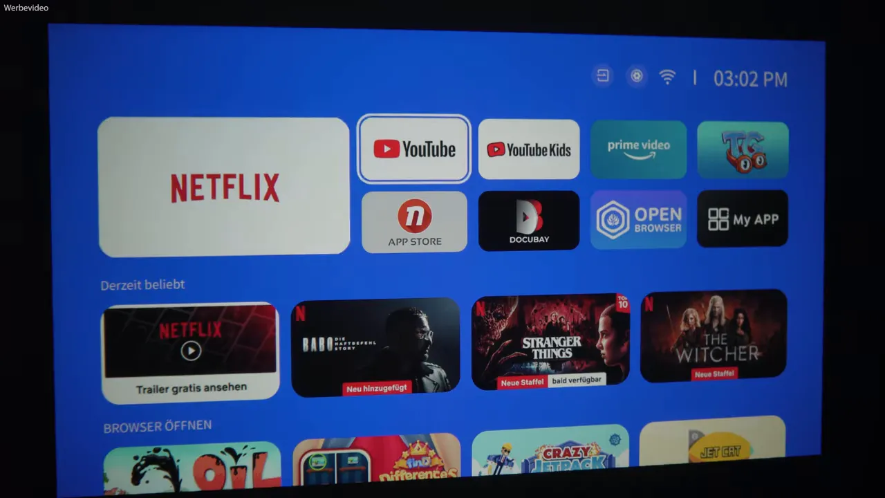 Projektionsbild des iWIMIUS P65 mit Netflix-, YouTube- und Prime-Icons auf Leinwand